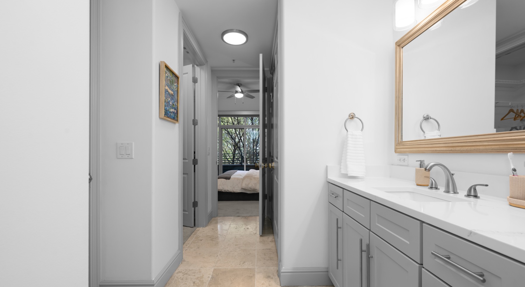 Apartment bathroom with long double vanity, large mirror, neutral tile flooring, and hallway layout leading to bedroom with balcony in Charlotte South End